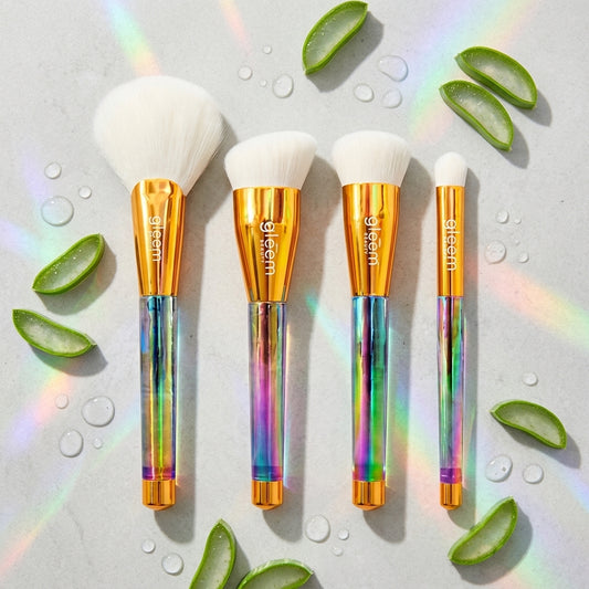 Gleem Beauty's ergonomic makeup brushes with rainbow handles and gold accents on a light background with aloe vera slices.